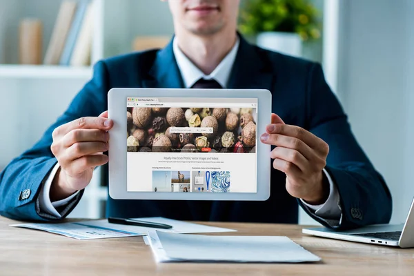 Kyiv, Ukraine - 8. Juli 2019: selektiver Fokus des Mannes mit digitalem Tablet mit Hinterlegungsfotos-App auf dem Bildschirm in der Nähe des Laptops im Büro — Stockfoto