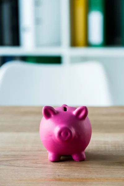 Pink toy piggy bank on wooden desk in office — Stock Photo