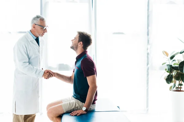 Arzt mit Brille schüttelt glücklichen Mann in Klinik die Hand — Stockfoto