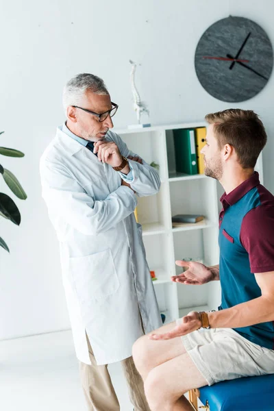 Pensive doctor in glasses looking at man showing shrug gesture — Stock Photo