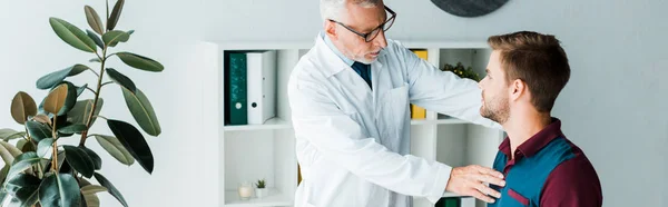 Tiro panorámico de médico en gafas tocando paciente - foto de stock