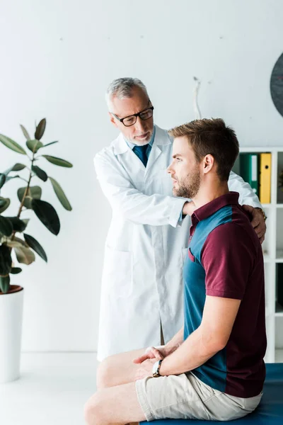 Medico in occhiali e camice bianco toccare bel paziente in clinica — Foto stock