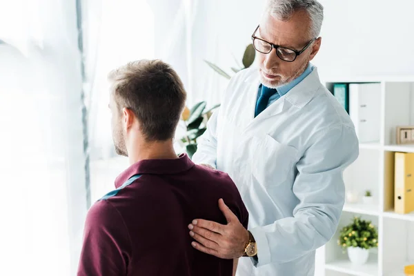 Doctor in glasses and white coat touching back of man in clinic — Stock Photo