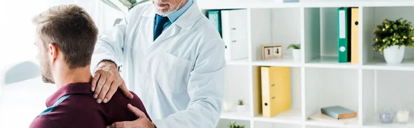 Colpo panoramico del medico in camice bianco che tocca la schiena dell'uomo in clinica — Foto stock