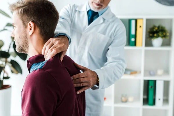 Cropped view of chiropractor in white coat touching back of patient in clinic — Stock Photo