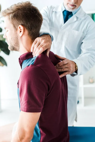 Vista recortada del quiropráctico en bata blanca tocando la parte posterior del paciente con los ojos cerrados — Stock Photo