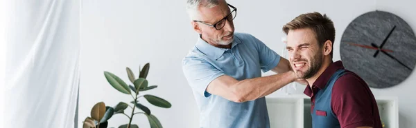 Panoramic shot of bearded man in glasses touching patient with pain in clinic — Stock Photo