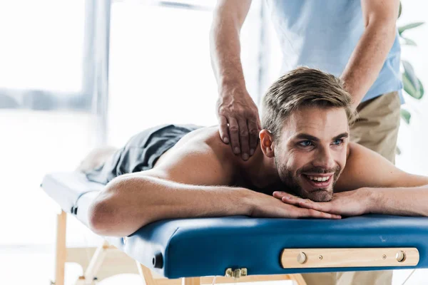 Обрезанный вид мануального терапевта, делающего массаж счастливому пациенту на массажном столе — стоковое фото