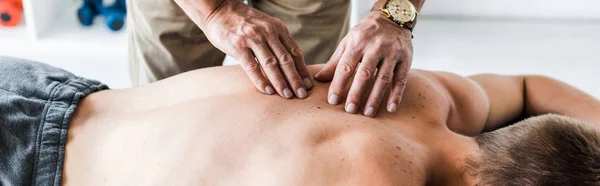 Tiro panorâmico de quiroprático fazendo massagem ao homem na mesa de massagem — Fotografia de Stock