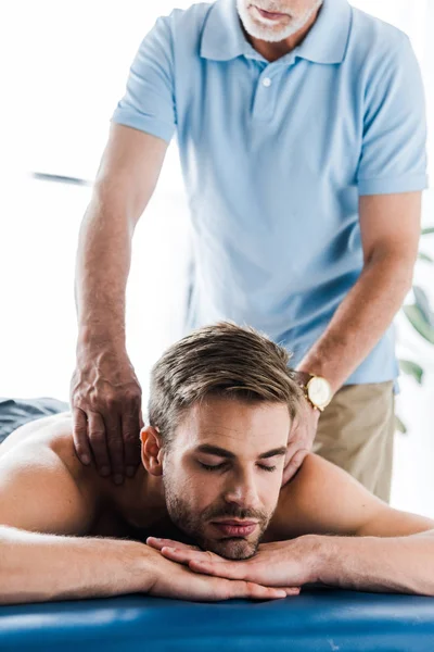 Visão cortada de quiroprático barbudo fazendo massagem ao paciente com os olhos fechados — Fotografia de Stock