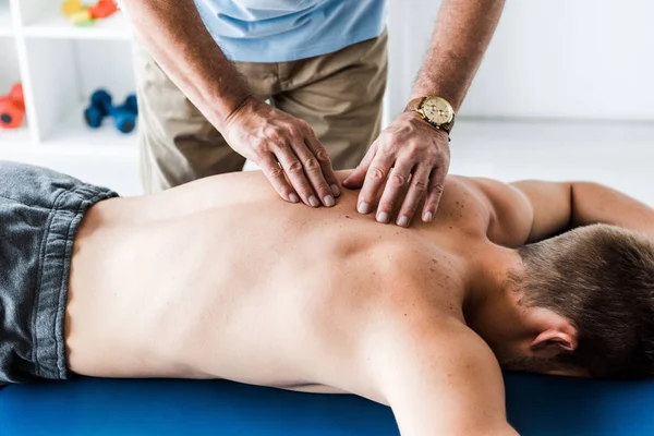 Recortado vista de quiropráctico haciendo masaje al hombre en mesa de masaje - foto de stock