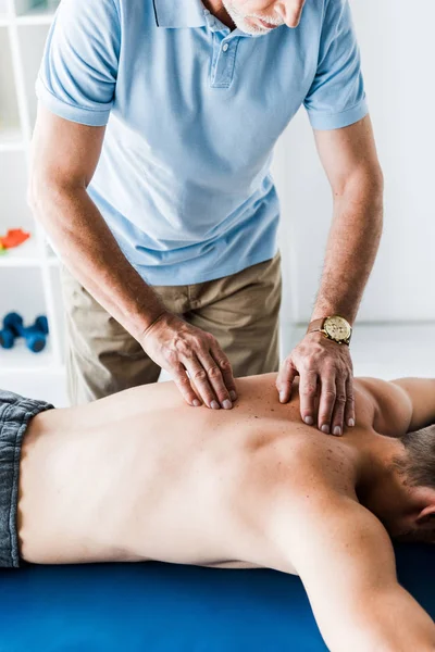 Обрізаний вид бородатого хіропрактика робить масаж пацієнту на масажному столі — стокове фото