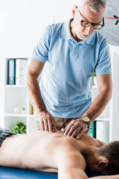 Quiropráctico barbudo haciendo masaje al paciente sin camisa en la mesa de masaje - foto de stock