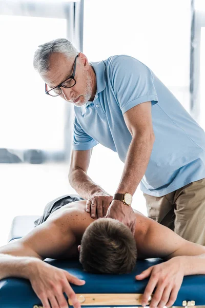 Bearded chiropractor doing massage to muscular patient on massage table — Stock Photo