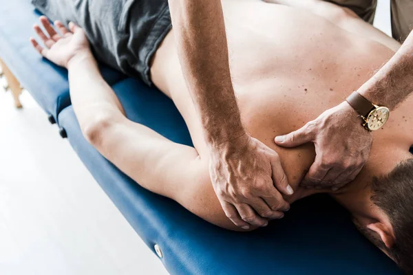 Vista cortada de quiroprático fazendo massagem ao homem sem camisa — Fotografia de Stock