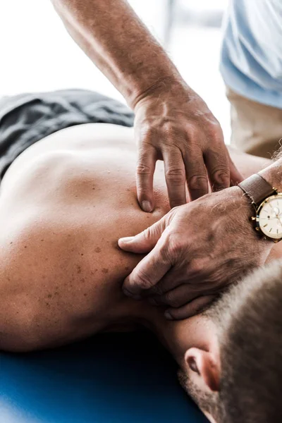 Enfoque selectivo del quiropráctico haciendo masaje al paciente sin camisa - foto de stock