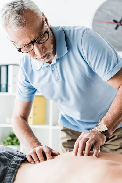 Bearded chiropractor in glasses doing massage to man on massage table — Stock Photo