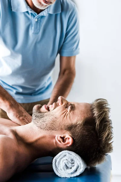 Cropped view of bearded chiropractor doing massage to man with pain — Stock Photo