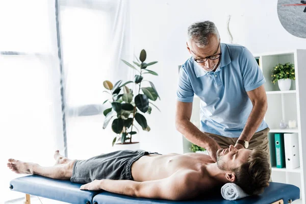 Бородатий хіропрактик робить масаж красивому чоловікові на масажному столі — стокове фото