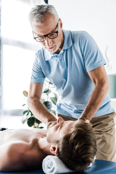 Selektiver Fokus des bärtigen Chiropraktikers bei der Massage des Mannes auf dem Massagetisch — Stockfoto