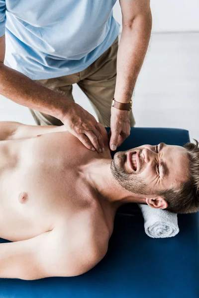 Overhead view of chiropractor doing massage to man with closed eyes suffering pain — Stock Photo