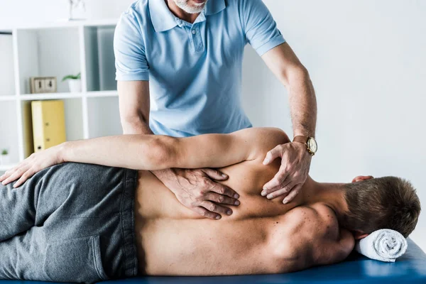 Vista recortada del quiropráctico tocando la espalda del hombre en la mesa de masaje - foto de stock