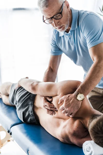 Handsome chiropractor touching back of patient on massage table — Stock Photo