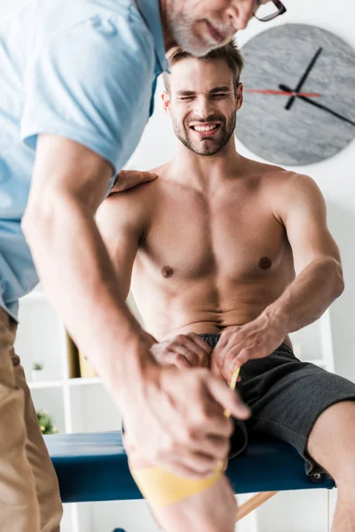 Ausgeschnittene Ansicht eines Arztes, der in der Nähe eines Mannes steht, der während der Reha mit Aufhängebändern trainiert — Stockfoto