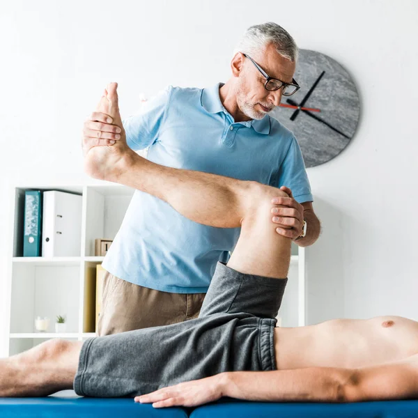 Cropped view of patient lying on massage table and working out near doctor in glasses — Stock Photo