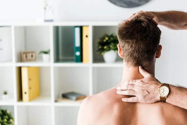 Cropped view of doctor touching neck of shirtless patient sitting in clinic — Stock Photo