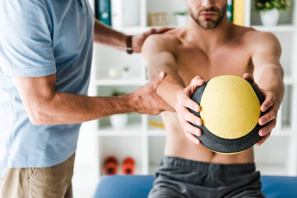 Cropped view of doctor standing near patient working out with ball — Stock Photo