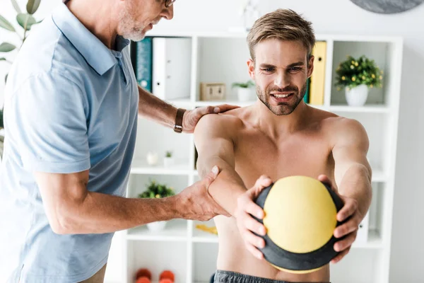 Ausgeschnittene Ansicht eines bärtigen Arztes, der neben einer Patientin steht, die mit Ball trainiert — Stockfoto