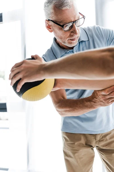 Selective focus of doctor in glasses looking at patient working out with ball — Stock Photo