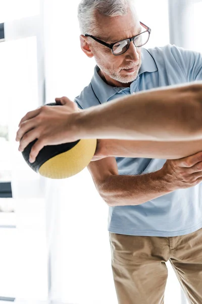 Enfoque selectivo del médico en gafas mirando al paciente haciendo ejercicio con pelota - foto de stock