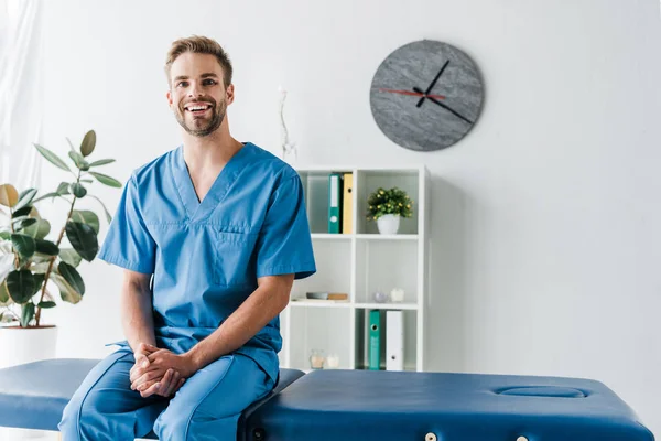 Médico alegre mirando la cámara mientras está sentado en la clínica - foto de stock