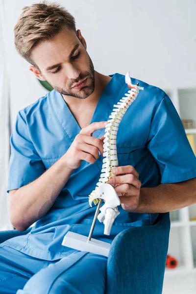 Bel medico toccante modello di colonna vertebrale mentre seduto in poltrona — Foto stock