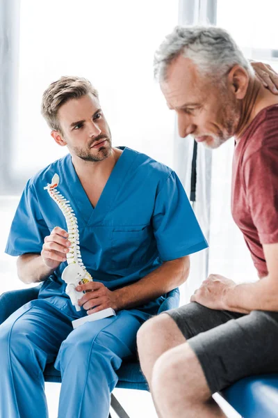 Selective focus of doctor holding spine model and looking at patient — Stock Photo