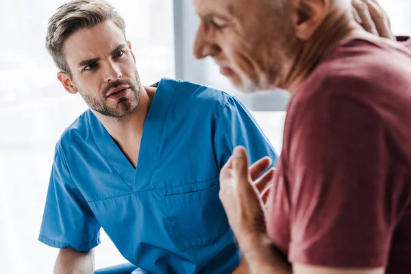 Selective focus of handsome doctor looking at man in clinic — Stock Photo