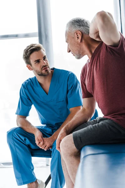 Selective focus of handsome doctor looking at man suffering from pain — Stock Photo