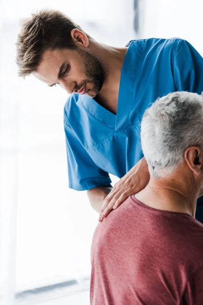 Selective focus of handsome doctor touching mature patient — Stock Photo