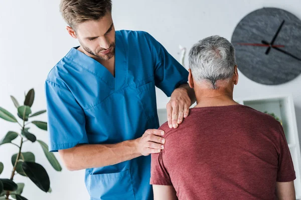 Vista posterior del paciente sentado cerca del médico guapo en la clínica - foto de stock