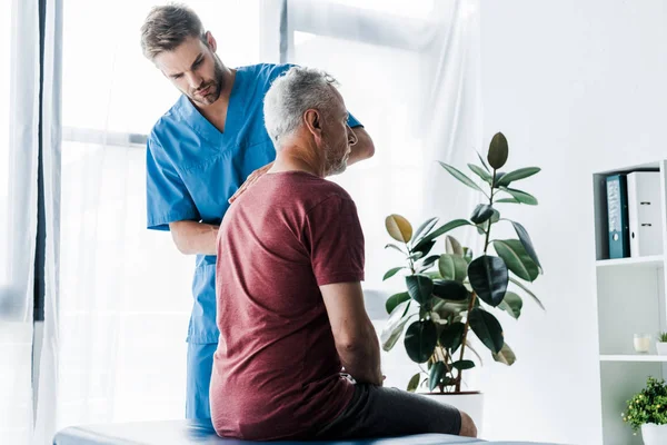 Schöner Chiropraktiker, der in der Nähe eines reifen Patienten steht — Stockfoto