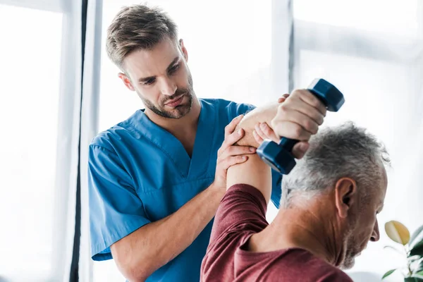 Selective focus of doctor near middle aged man exercising with dumbbell — Stock Photo
