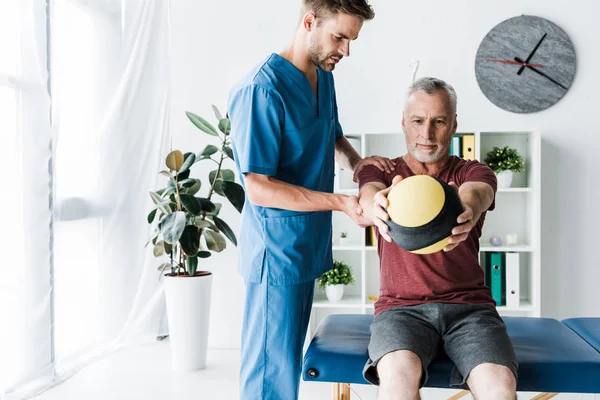 Selective focus of mature man training with ball near doctor — Stock Photo