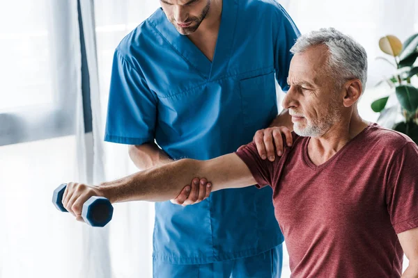 Cropped view of doctor standing near mature man holding dumbbell in clinic — Stock Photo