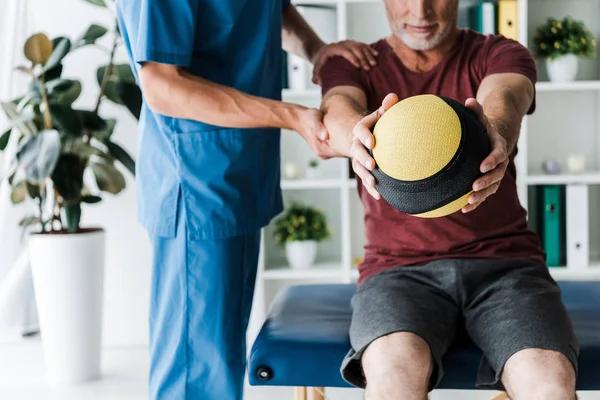 Обрезанный вид взрослого человека тренировки с мячом рядом с врачом — стоковое фото