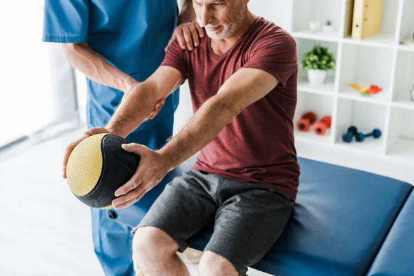 Селективный фокус бородатый мужчина среднего возраста упражнения с мячом рядом с врачом — стоковое фото