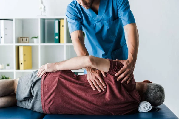 Recortado vista de médico tocando hombre de mediana edad acostado en mesa de masaje - foto de stock