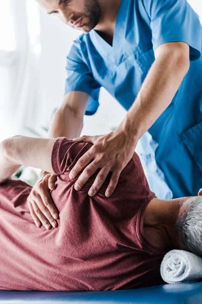 Selective focus of doctor touching middle aged man lying on massage table — Stock Photo