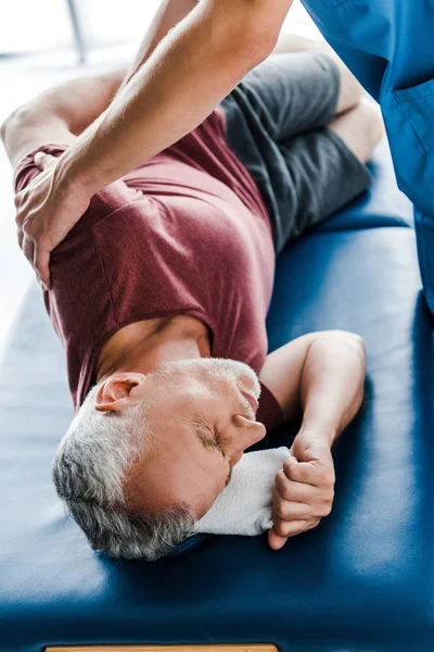 Selektiver Fokus des Arztes berührt Mann mittleren Alters mit geschlossenen Augen, der auf Massagetisch liegt — Stockfoto